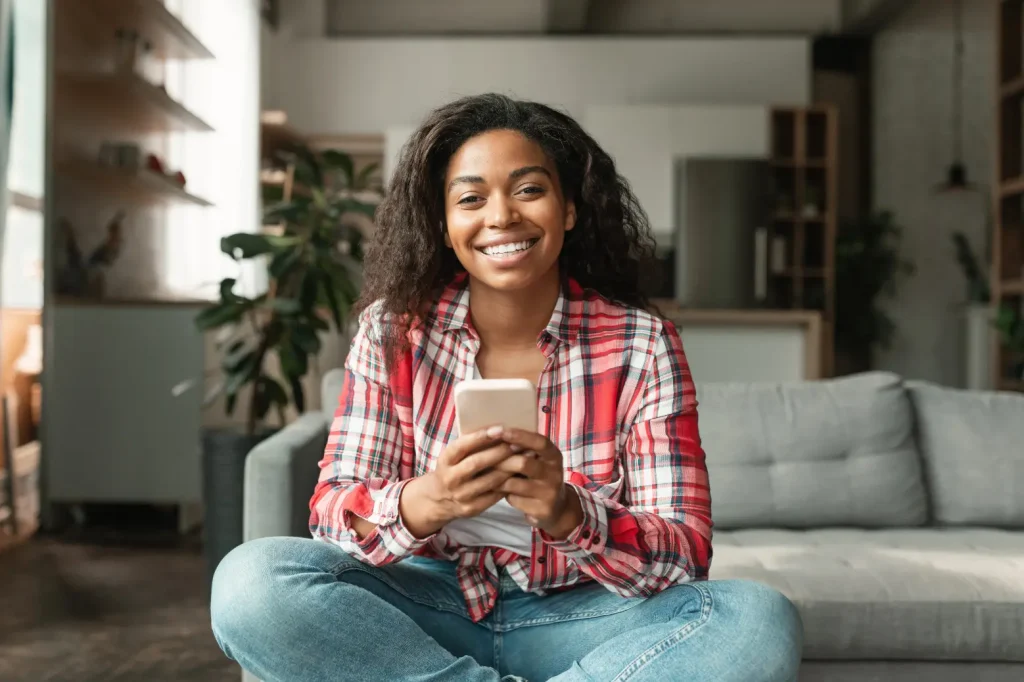 Jane Swyft sitting on a sofa, smiling and holding her phone, ready to confirm a mobile notary appointment.
